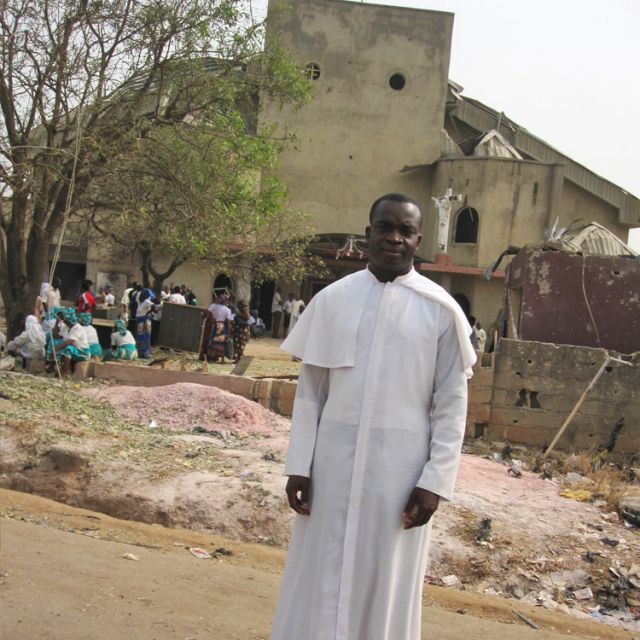 Fr. Emmanuel-Mary Mbam stands outside St. Theresa’s Church after the Christmas Day bombing attack.