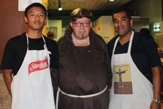 Br. John Frampton is flanked by volunteers Sonny Doria (left) and Lionel Alleluia at St. Francis Table. 