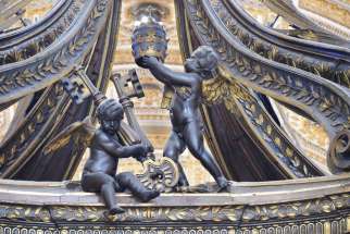 A cherub holding the keys of St. Peter and one holding up a papal tiara can be seen in this close-up photograph of the wooden canopy of the baldachin over the main altar of St. Peter’s Basilica.