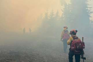 Firefighters are seen in an undated photo walking through smoke from wildfires near High Prairie, Alta.