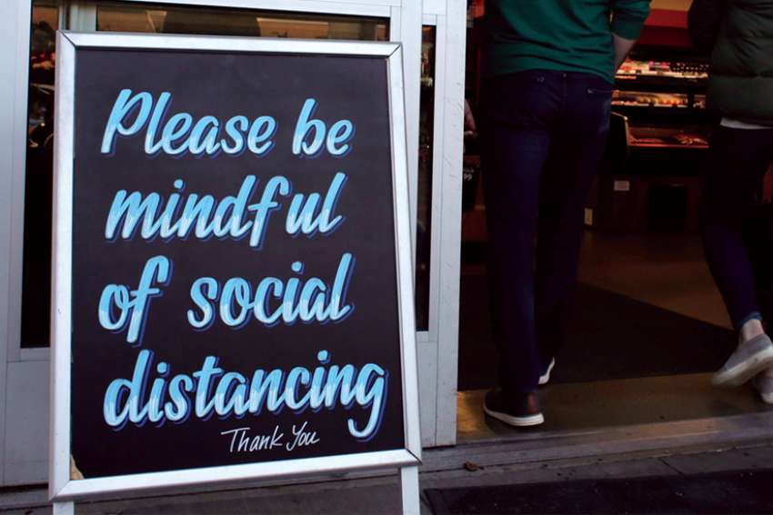 Shoppers enter a grocery store  with a reminder to keep their distance.
