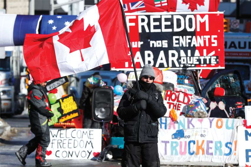 A person waves a Canadian flag in front of banners in support of truckers during the Freedom Convoy rally in Ottawa in February.