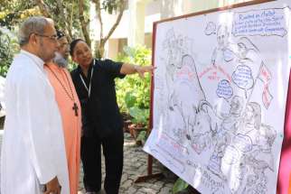 Bishop Stephen Rotluanga of Aizawl, India, explains his cartoon on the conference to Cardinal Baselios Cleemis Thottunkal in Bangalore March 9.
