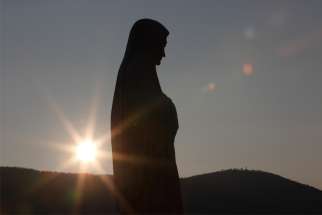 The sun sets behind a statue of Mary on Apparition Hill in Medjugorje, Bosnia-Herzegovina, in this Feb. 26, 2011, file photo. Senior Vatican representatives joined dozens of bishops and hundreds of priests at the first officially approved church youth festival at the site Aug. 2-6, 2019, three months after Catholic pilgrimages were authorized by the pope.