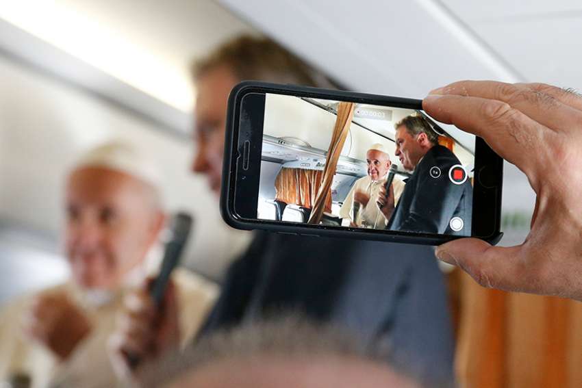  Pope Francis is pictured on a cell phone video with Vatican spokesman, Greg Burke, as he greets journalists aboard his flight from Rome to Vilnius, Lithuania, Sept. 22. 