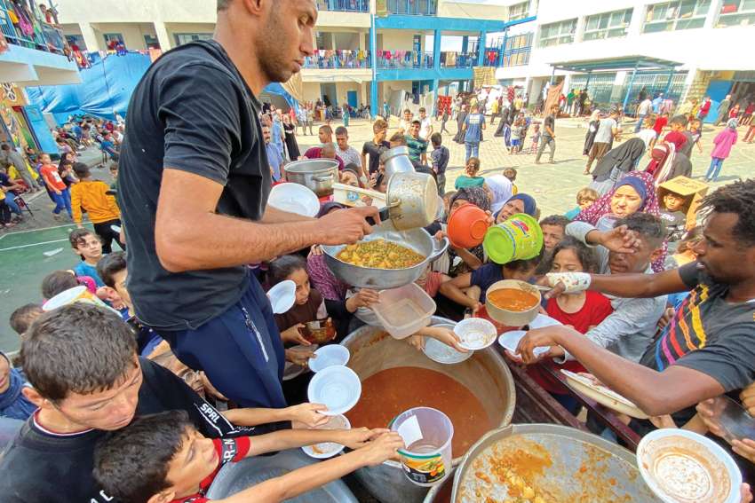 Palestinians who fled their houses due to Israeli airstrikes gather to receive food offered by volunteers at a UN-run school where they have taken taken refuge in Rafah, in the southern Gaza Strip.