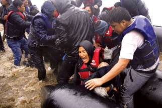 An Afghan mother holds her baby as she struggles to disembark a raft during a rainstorm in Lesbos, Greece, Oct. 23. The Canadian bishops have called for urgent action to aid refugees.