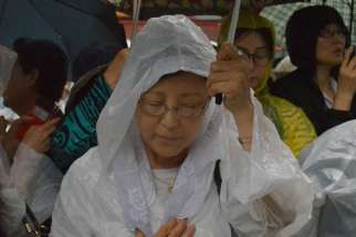 A woman prays with others in the rain outside Myongdong Cathedral in Seoul, South Korea, as Pope Francis celebrates a Mass for peace and for the reconciliation of North and South Korea inside Aug. 18. Many Catholic and non-Catholics braved the pouring ra in to try to get a glimpse of the pontiff at his last Mass before leaving South Korea.