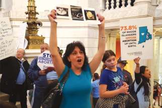 Diane Pennine holds photos of her daughter’s ultrasound in the Rhode Island Statehouse to protest a bill aimed at expanding legal abortion. Hundreds of activists erupted into cheers as news spread that the bill was voted down.