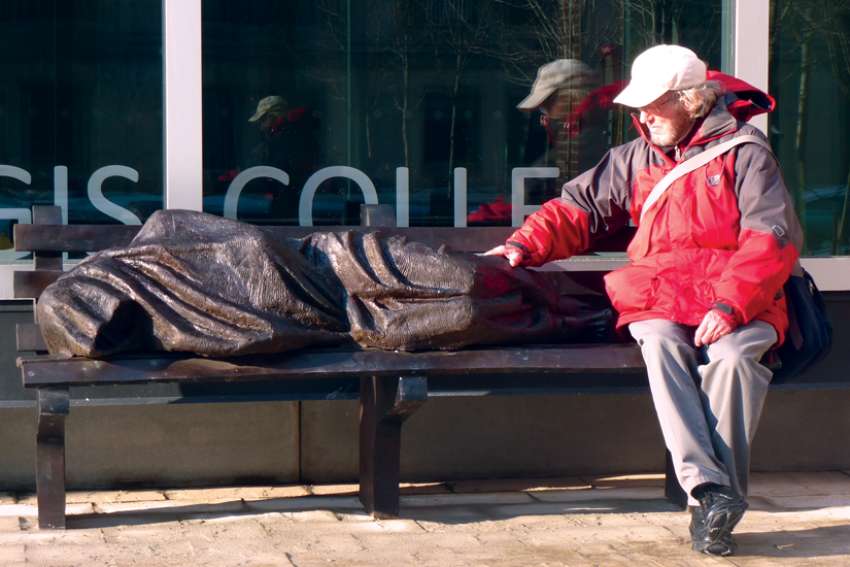 Fr. Peter Larisey has a seat with Homeless Jesus at Regis College.