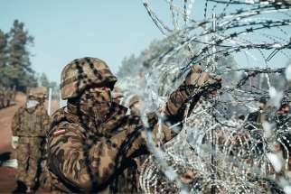 A Polish soldier installs barbed wire on the Poland-Belarus border near Kuznica, Poland, Nov. 9, 2021. Poland deployed 15,000 troops with razor wire and tear gas and announced plans for a 65-mile border wall after stranded migrants, mostly from Asia and the Middle East, amassed at the border.