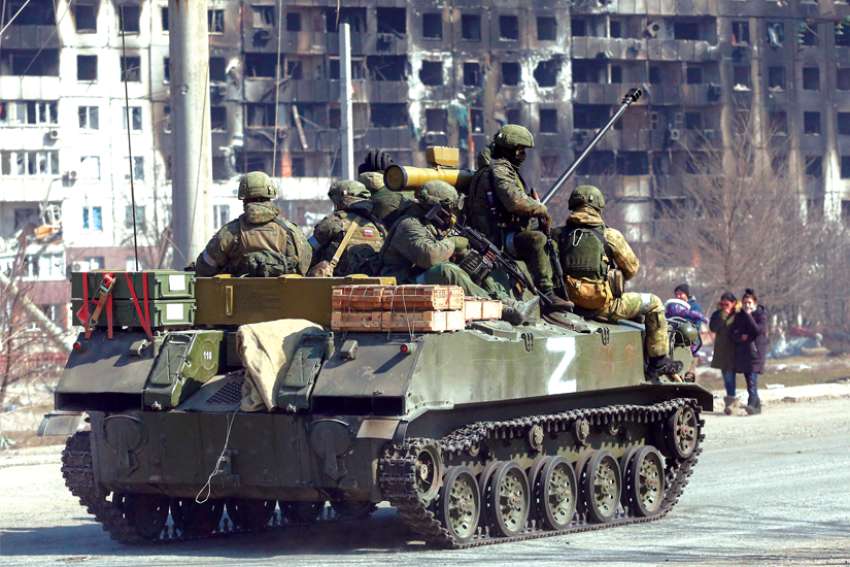 Service members of pro-Russian troops in the besieged southern port city of Mariupol, Ukraine, are seen atop an armored vehicle with the symbol “Z” painted on its side.