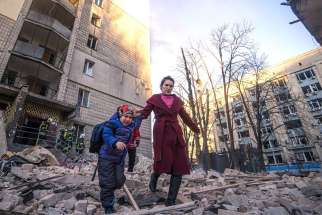 A woman with a child evacuates from a residential building damaged by Russian shelling in Kyiv, Ukraine, March 16, 2022.