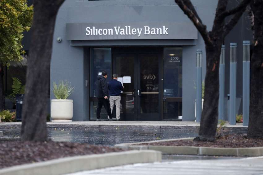 A man puts a sign on the door of the Silicon Valley Bank as an onlooker watches at the bank’s headquarters in Santa Clara, Calif., March 10, 2023.