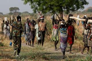 A soldier walks past women carrying their belongings Feb. 11 near Bentiu, South Sudan. South Sudan&#039;s Catholic bishops have denounced government and rebel troops for attacking the civilian population and at times operating &quot;scorched-earth&quot; policies in defiance of international law.