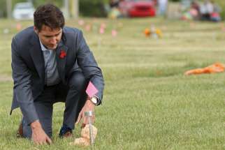 Prime Minister Justin Trudeau places a teddy bear at an unmarked grave as he visits the Cowessess First Nation near Grayson, Sask., July 6.