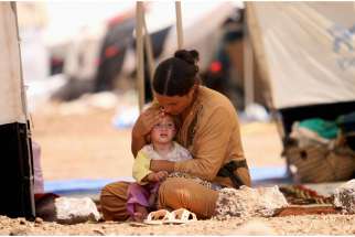 A woman who fled the violence in the Iraqi town of Sinjar sits with a child inside a tent at a camp in Syria&#039;s northern town of Qamishli Aug. 17, 2014.