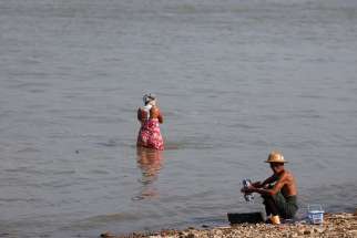 A man washes clothes and a woman washes her hair along the bank of the Irrawaddy River in Sagaing, Myanmar, March 4, 2012. The Irrawaddy River is &quot;our mother&quot; and is at risk of being lost &quot;to the greed of a superpower,&quot; Cardinal Charles Maung Bo of Yangon said in a Jan. 28 statement. 