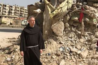 Father Michael Perry, minister general of the Franciscans, walks past the rubble of a bombarded building in Aleppo, Syria, during an early April visit to Franciscan friars there.