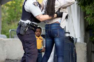  Two-year-old Evanston, whose family stated they are from Haiti, watches as a Royal Canadian Mounted Police officer pats down his mother before the two cross the U.S.-Canada into Quebec Aug. 29, 2017.