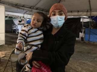 Adalia Reyes, an asylum-seeker from El Salvador, poses with a friend&#039;s child outside a Mass celebrated Jan. 9, 2021, in a tent camp for migrants along the U.S.-Mexico border in Matamoros. Reyes said, out of desperation, she sent her two children unaccompanied to the United States, where they were reunited with their father.