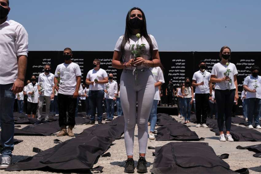 Students affiliated with the Lebanese Forces hold white roses and stand next to body bags in Beirut Aug. 4 in memory of victims of the 2020 Beirut port explosion. Pope Francis is urging the international community to help Lebanon with concrete action so it may rise again as sign of peace and fraternity for the Middle East.