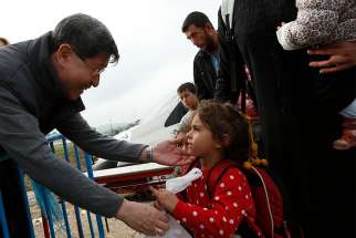 Cardinal Luis Antonio Tagle of Manila gives a food bag to a refugee family as they arrive at a transit camp in Idomeni, Greece, on the border of Macedonia Oct. 19. Thousands of refugees are arriving into Greece from Syria, Afghanistan, Iraq and other countries and then traveling further into Europe in 2015. 