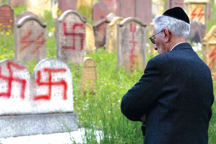 A member of the Jewish community views anti-Semitic graffiti on tombstones at a Jewish cemetery.