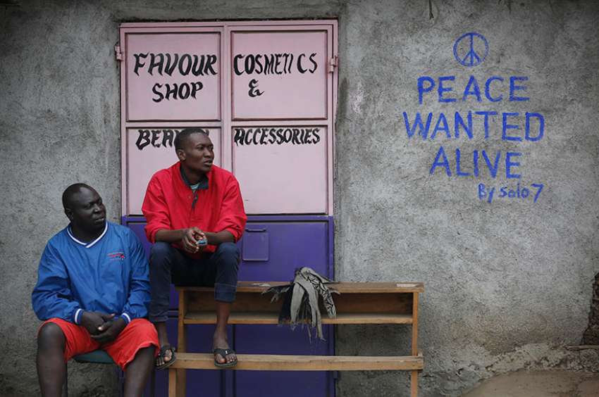 Men sit in front of a wall with a message of peace July 23 in Nairobi, Kenya. Kenyan Catholic bishops have urged citizens to prepare to vote peacefully in the Aug. 8 general elections.