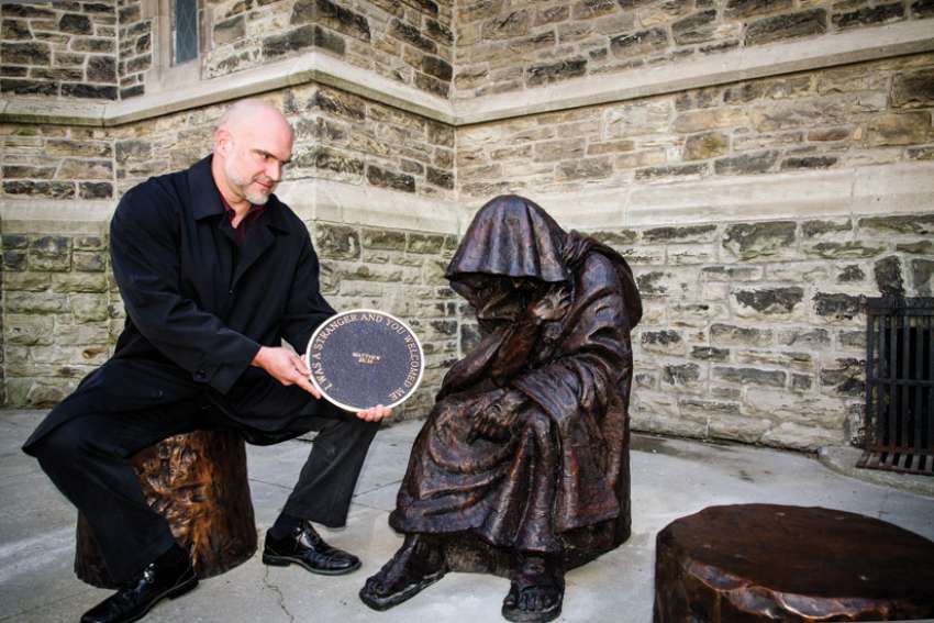 Catholic sculptor Timothy Schmalz sits next to his recently unveiled statue, When I Was a Stranger, at Toronto’s St. Paul’s Anglican Church.