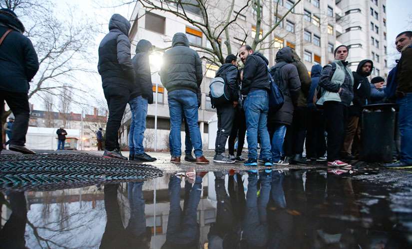Migrants are reflected in a puddle as they queue in front of the Berlin Office of Health and Social Affairs for their registration process, early morning of Feb. 2, 2016.
