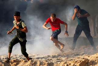 Palestinian youths run for cover from tear gas fired by Israeli troops during a Sept. 10 protest along a beach in the Gaza Strip. The U.S. budgetary cuts to humanitarian aid institutions providing assistance to Palestinians in Gaza and the West Bank could lead to long-term disastrous consequences, said aid workers in the region.