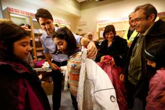 Prime Minister Justin Trudeau helps a young Syrian refugee try on a winter coat at the Toronto Pearson International Airport December 2015. Private and government sponsorship funds to support refugee families for a year are coming to a end.