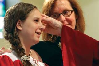 A young girl is anointed during Confirmation while her sponsor looks on.