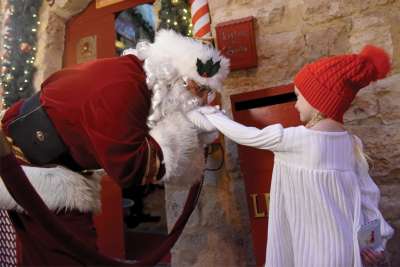 Palestinian Catholic Issa Kassissieh, known as Jerusalem Santa, wearing a protective mask, kisses the hand of four-year-old Mia Tusko at the entrance to Santa’s House Dec. 7. The house was created out of his family’s 700-year-old home in the Old City of Jerusalem.