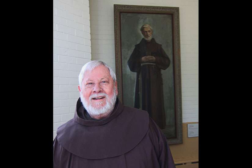 Fr. Roland Bonenfant, director of the Frédéric Jansoone Centre in Trois Rivieres, Que., stands in front of a painting of the Franciscan who was beatified by Pope John Paul II in 1988.