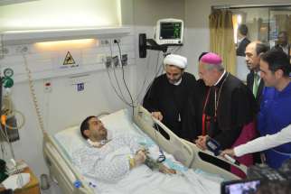 Vatican&#039;s nuncio to Lebanon, Archbishop Gabriele Caccia, centre, visits a hospitalized victim of the Nov. 12 twin suicide bombings in Beirut. Fr. Wissam Maalouf, founder and superior of Mission of Life, is at right.