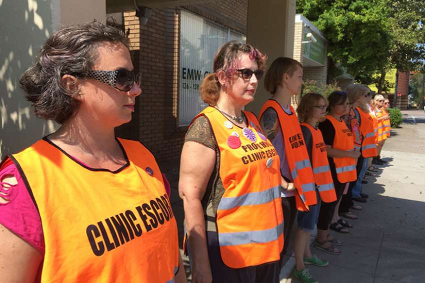 In this Monday, July 17, 2017 photo, Meg Stern, left, and other escort volunteers lined up outside the EMW Women&#039;s Surgical Center in Louisville, Ky. A federal judge issued an order Friday, July 21, 2017, to keep protesters away from a &quot;buffer zone&quot; outside Kentucky&#039;s only abortion clinic, which is targeted by a national anti-abortion group. 