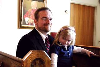 Mark Siolek, chaplain at Msgr. Percy Johnson Catholic High School, with his daughter, Madeline, sits in the pews he salvaged for the school chapel.