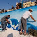 Workers paint waves on a mural in front of the altar July 7 Lampedusa, Italy. Pope Francis will celebrate Mass and pray for immigrants lost at sea when he visits the island July 8. Located about 70 miles from Tunisia, the island has been the destination for thousands of African immigrants seeking a better life in Europe.