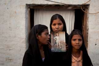 The daughters of Asia Bibi, a Catholic eventually aquitted of blasphemy, pose in 2010 with an image of their mother while standing outside their residence in Sheikhupura, Pakistan. Bibi, the Pakistani Catholic mother freed after eight years on death row, says people must help Pakistanis falsely implicated in blasphemy cases get released.