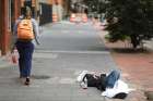 A woman walks past a homeless man sleeping on a sidewalk. We are called to not turn our faces from the poor.