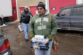 Flint resident Ruby Adolph carries bottled water and a replacement water filter she received at a fire station in Flint, Mich., on Jan. 13, 2016. 