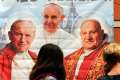 A woman takes a picture of an illustration depicting Blessed John Paul II, left, Pope Francis and Blessed John XXIII outside a shop in Rome April 23.  Pope Francis expressed his hopes that the two soon-to-be saints would continue to inspire the whole church in its mission.