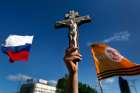 A pro-Russian man holds a crucifix next to a Russian flag during a demonstration in Donetsk&#039;s Lenin Square May 24 against the Ukrainian elections. Bishop Marian Buczek said church members are afraid to attend Mass in Donetsk and other towns after a priest was abducted by pro-Russia separatists.