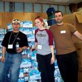 From left to right, volunteers Dan Chiarello, Shannon Hobbs and Patrick Simonaitis stand in front of hundreds of bottles of donated water in the basement of St. Peter’s Church.