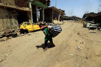 A boy carries his belongings in Mosul, Iraq, July 23. Some Iraqi Christians who are making their slow return to ancestral lands say it will take time to rebuild their lives and trust of those who betrayed them.