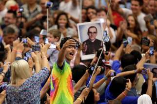 An audience member takes a selfie of himself with a photo of Blessed Oscar Romero behind him as Pope Francis arrives to lead his general audience in Paul VI hall at the Vatican Aug. 3. Bishops from Panama say Blessed Romero is an example of faith for youths.
