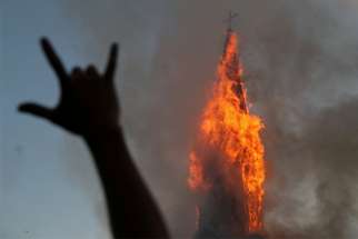 A protester gestures while a church is set on fire during a demonstration against Chile&#039;s government in Santiago Oct. 18, 2020, the one-year anniversary of the protests and riots that rocked the capital in 2019. The current protests occurred a week before a referendum on whether to ditch a dictatorship-era constitution.