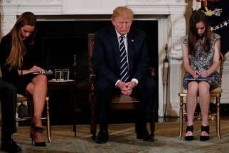 President Donald Trump bows his head during a prayer as he sits between Marjory Stoneman Douglas High School shooting survivors and students Julia Cordover and Carson Abt Feb. 21 at the White House. Trump hosted the listening session with high school students. families and teachers to discuss school safety in the wake of a mass shooting a week earlier at the school in Parkland, Fla.